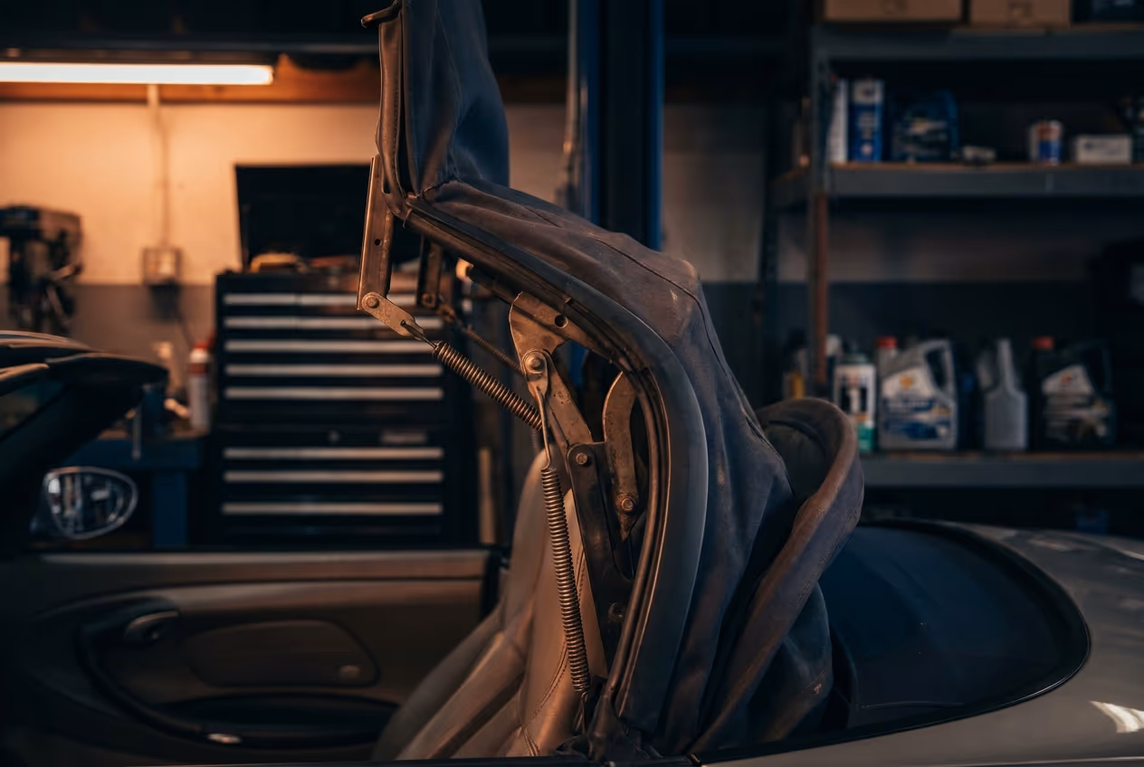 Teilweise geöffnetes Stoffverdeck eines Porsche Boxster mit sichtbarer Verdeckmechanik in einer Werkstatt